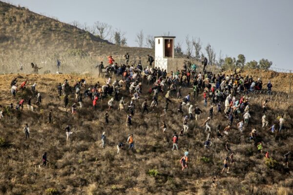 Migrants storm a barbed-wire fence as they attempt to cross the land border with Spain