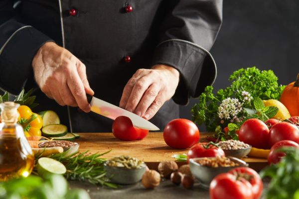 A chef in a black apron cuts colorful vegetables on a cutting board.