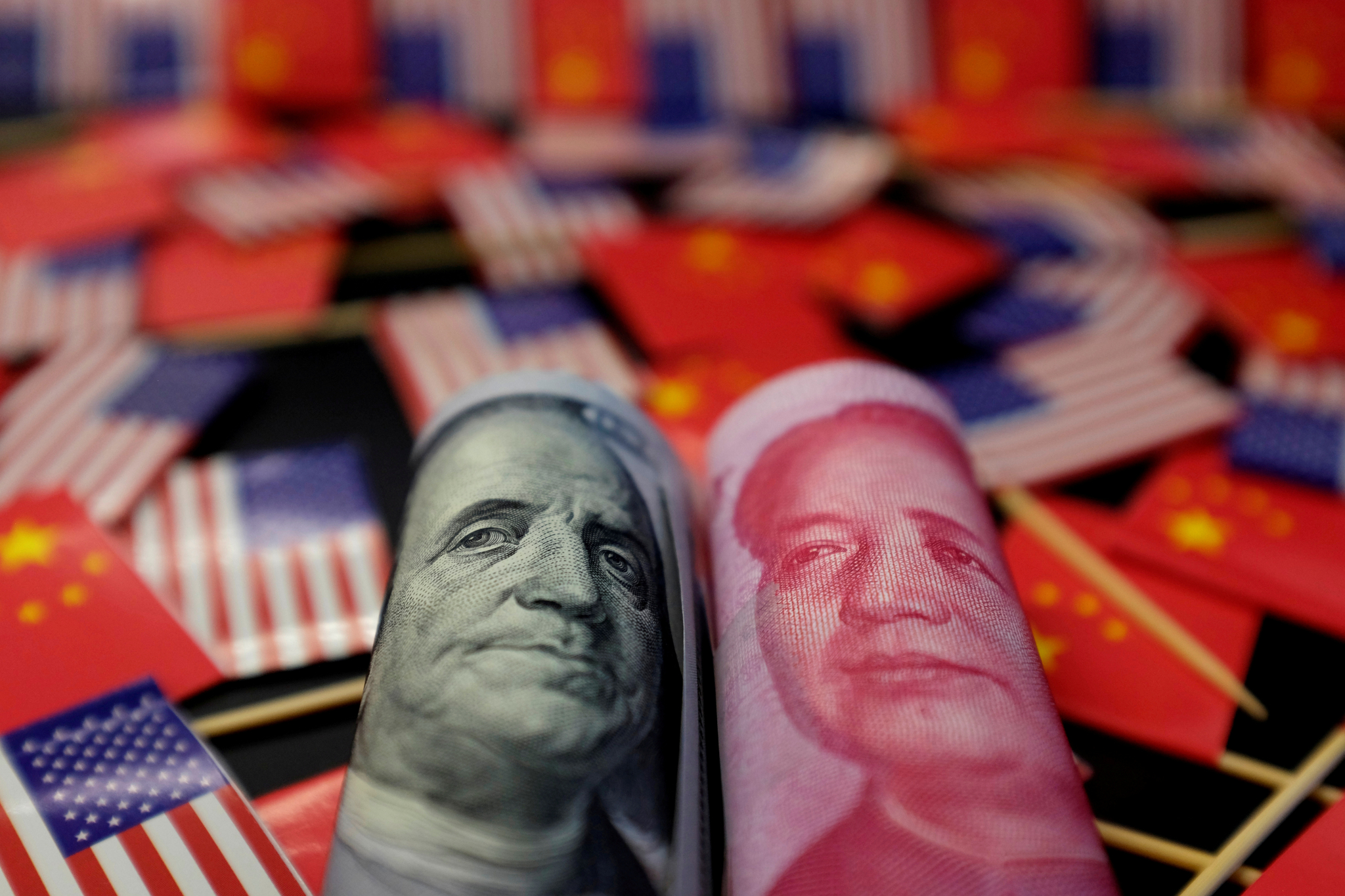 A U.S. dollar banknote featuring U.S. founding father Benjamin Franklin and China's yuan banknote featuring late Chinese chairman Mao Zedong are seen among U.S. and Chinese flags [REUTERS/YONHAP]