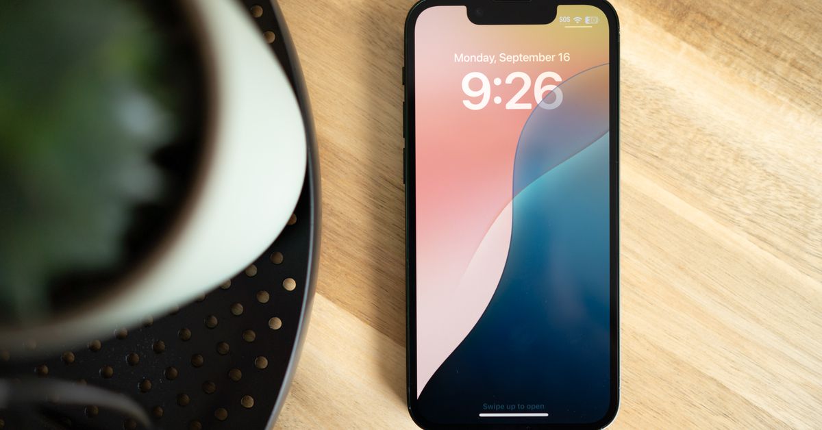 Photo of iPhone with iOS 18 wallpaper on a wooden table.