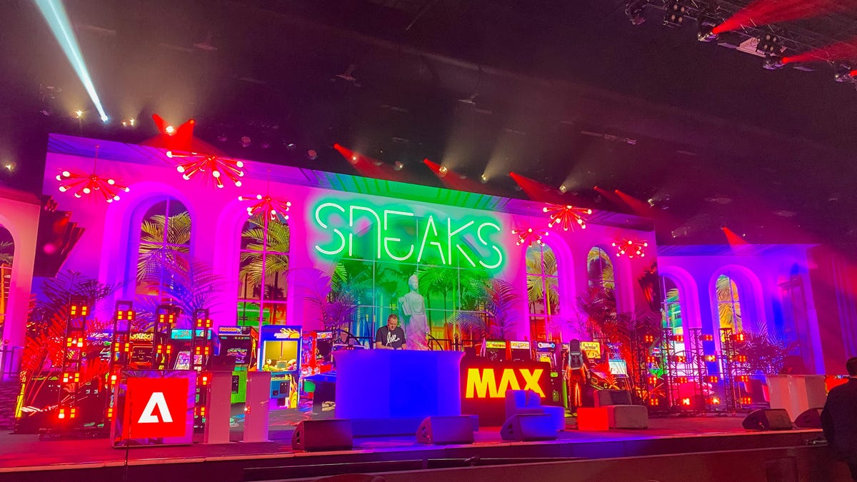 a brightly lit stage with a DJ playing with the word "sneaks" in neon green above the DJ