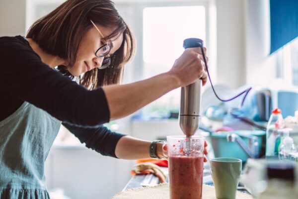 Woman makes a fruit smoothie with an immersion blender.