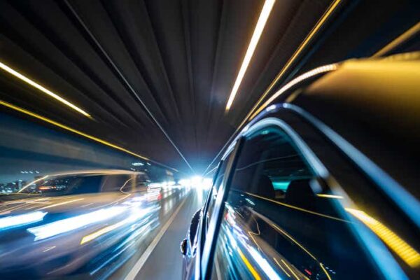 Fast driving hybrid car on crowded, illuminated city street.