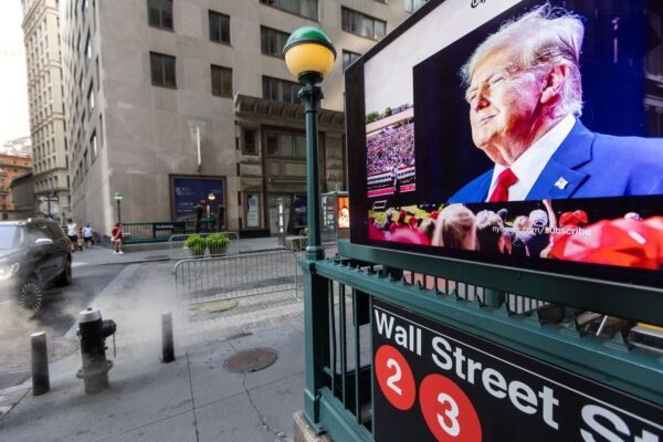 A screen displays an image of Donald Trump at a Wall Street subway station.