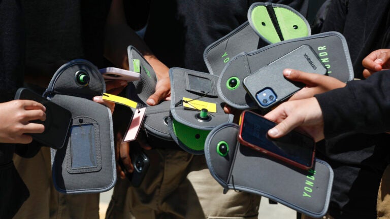A student uses their cell phone after unlocking the pouch that secures it from use during the school day.