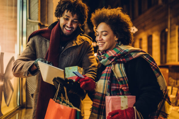 Smiling young couple buying Christmas presents online using a credit card and a digital tablet.