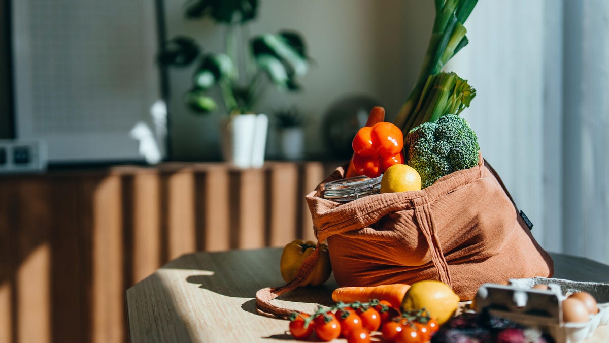 Eco-friendly reusable shopping bag with multi-coloured fresh vegetables and groceries on the table at home