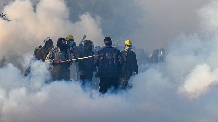 Protesters wearing masks and helmets walk through thick clouds of tear gas in Islamabad