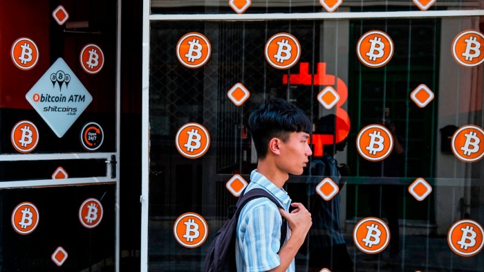 A man with a backpack walks past a storefront displaying multiple Bitcoin symbols and an advertisement for Bitcoin ATMs in Nicosia.