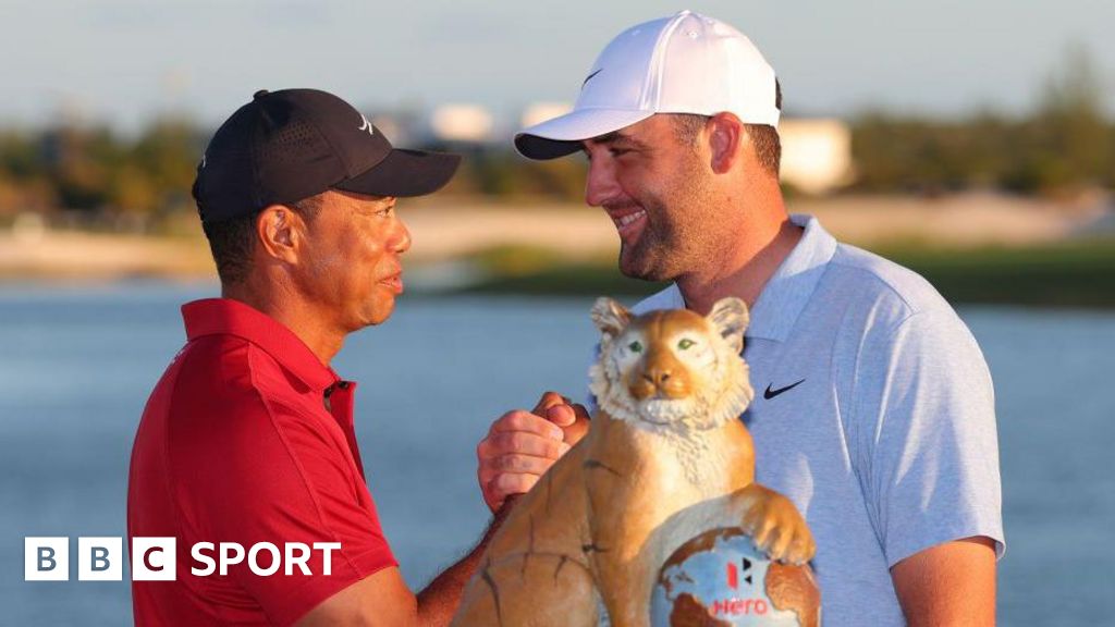 Host Tiger Woods shakes hands with winner Scottie Scheffler at the 2024 Hero World Challenge event, beside the tournament trophy