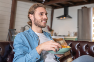 Man sitting on couch eating from bowl of chips