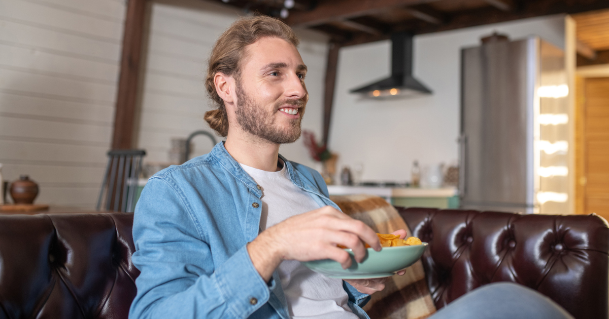 Man sitting on couch eating from bowl of chips