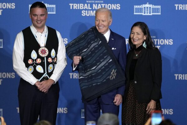 Interior Secretary Deb Haaland, right, and Bryan Newland, Assistant Secretary for Indian Affairs at the Department of the Interior, left, present President Joe Biden with an Eighth Generation blanket from a tribally-owned business, embroidered with "Joe Biden Champion for Indian Country," at the 2024 White House Tribal Nations Summit at the Department of the Interior in Washington, Monday, Dec. 9, 2024. (AP Photo/Susan Walsh)