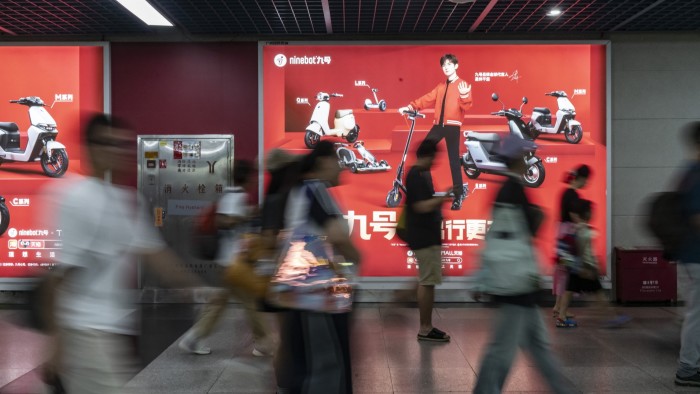 Commuters walk past an advertisement for electric motorcycles at a busy subway station in Guangzhou