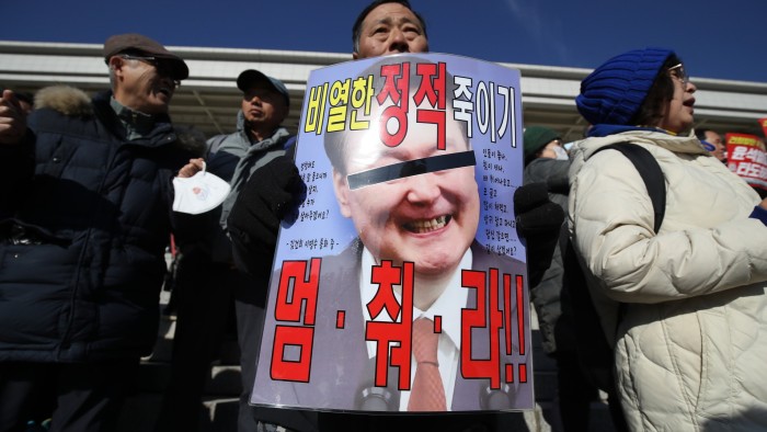 A protester prominently displays a sign featuring an image of Yoon Suk Yeol with a black bar over his eyes