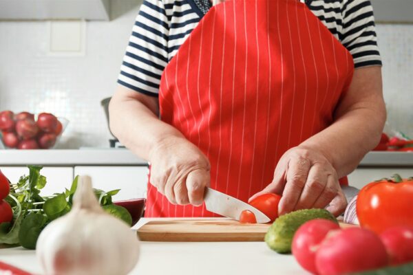 A photo of a mature woman slicing a tomato in her kitchen.