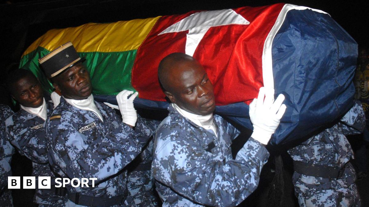 Four gendarmes, wearing blue digital camouflage fatigues and white gloves, carry a coffin bearing the Togolese flag on their shoulders