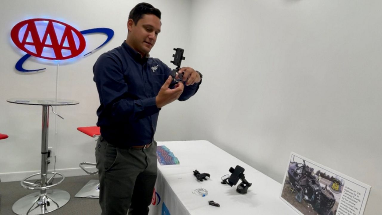 Nick Chabarria, spokesperson for AAA, describes how to use a variety of cellphone mounts that people can use in their cars Monday morning. The new Missouri "Siddens Bening Hands Free" law went into effect, which prohibits all drivers from manually typing, scrolling or holding a cellphone or another wireless device while their car is in motion. (Spectrum News/Elizabeth Barmeier)