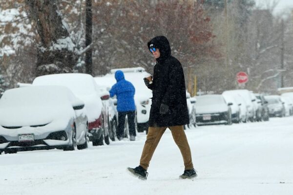 A pedestrian crosses First Avenue as a winter storm sweeps over the intermountain West, plunging temperatures into the single digits and bringing along a light snow in its wake Saturday, Jan. 18, 2025, in Denver. (AP Photo/David Zalubowski)