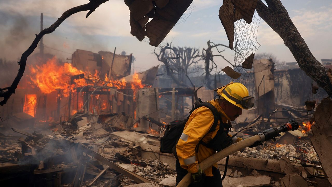 A firefighter battles the Palisades Fire around a burned structure in the Pacific Palisades neighborhood of Los Angeles, Jan. 8, 2025. (AP Photo/Etienne Laurent)