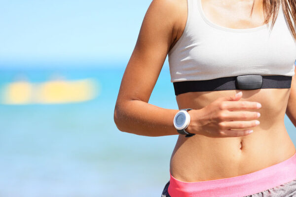 How health elevates your luxury lifestyle potential Runner woman with heart rate monitor running on beach with watch and sports bra top. Beautiful fit female fitness model training and working out outside in summer at part of healthy lifestyle.