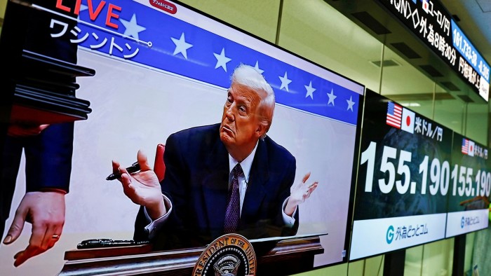 A broadcast of US President Donald Trump next to screens displaying the current Japanese Yen exchange rate against the dollar