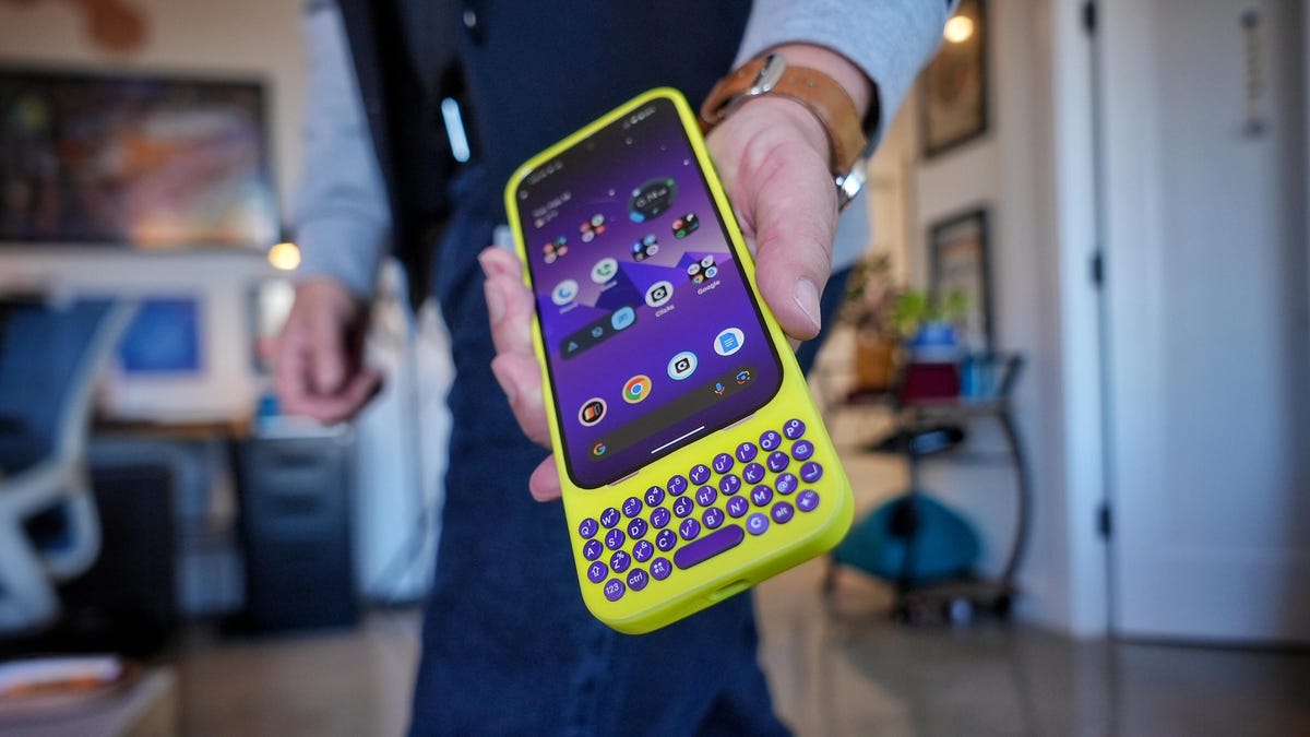 A man holds out a phone wrapped in a case with a physical keyboard protruding from the bottom.