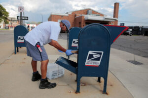 A United States Postal Service (USPS) worker handles the mail in a drop-off box behind a post office in Oak Park, Michigan...