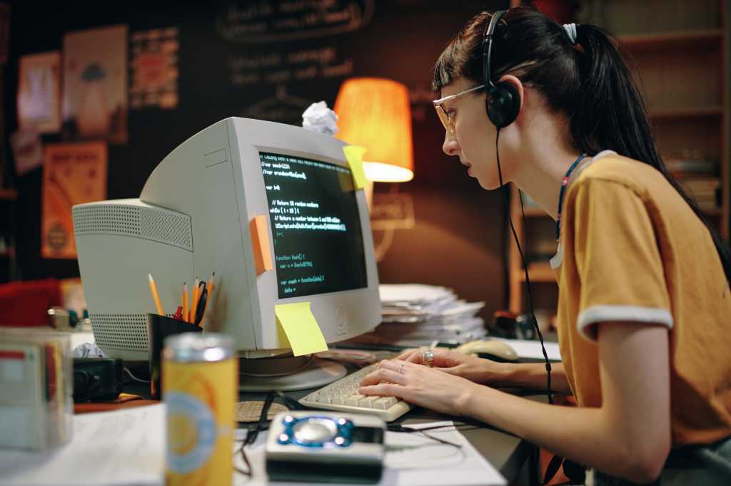 Young woman in headphones typing codes for new software on computer, she working at her workplace in garage