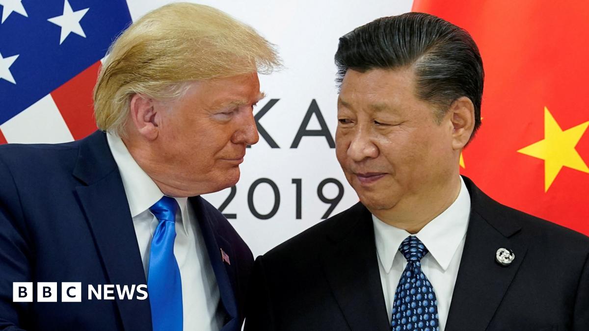 U.S. President Donald Trump meets with China's President Xi Jinping. They are both wearing suits, and standing very close to one another. Behind them, the flags of their countries and a white sign saying 2019