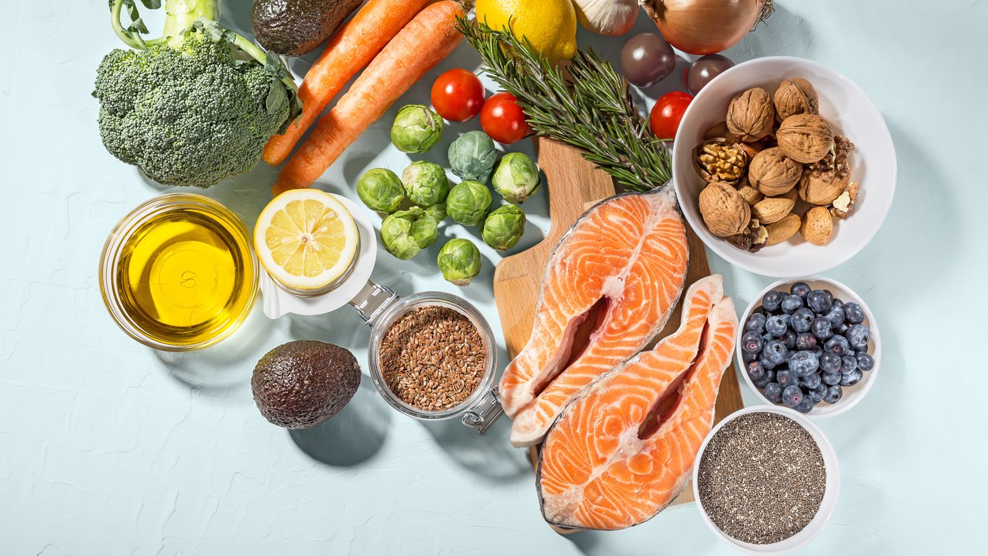 a variety of health fresh fruits and vegetables along with olive oil, salmon, walnuts, avocados, chia and flax seeds shot from above