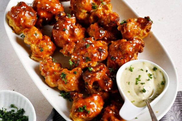40+ Vegan Super Bowl Recipes: Snacks and More hand grabbing a vegan Buffalo cauliflower wing as Superbowl snack