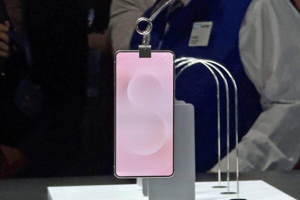 A phone with a pink screen background hangs from a clip on a display floor.