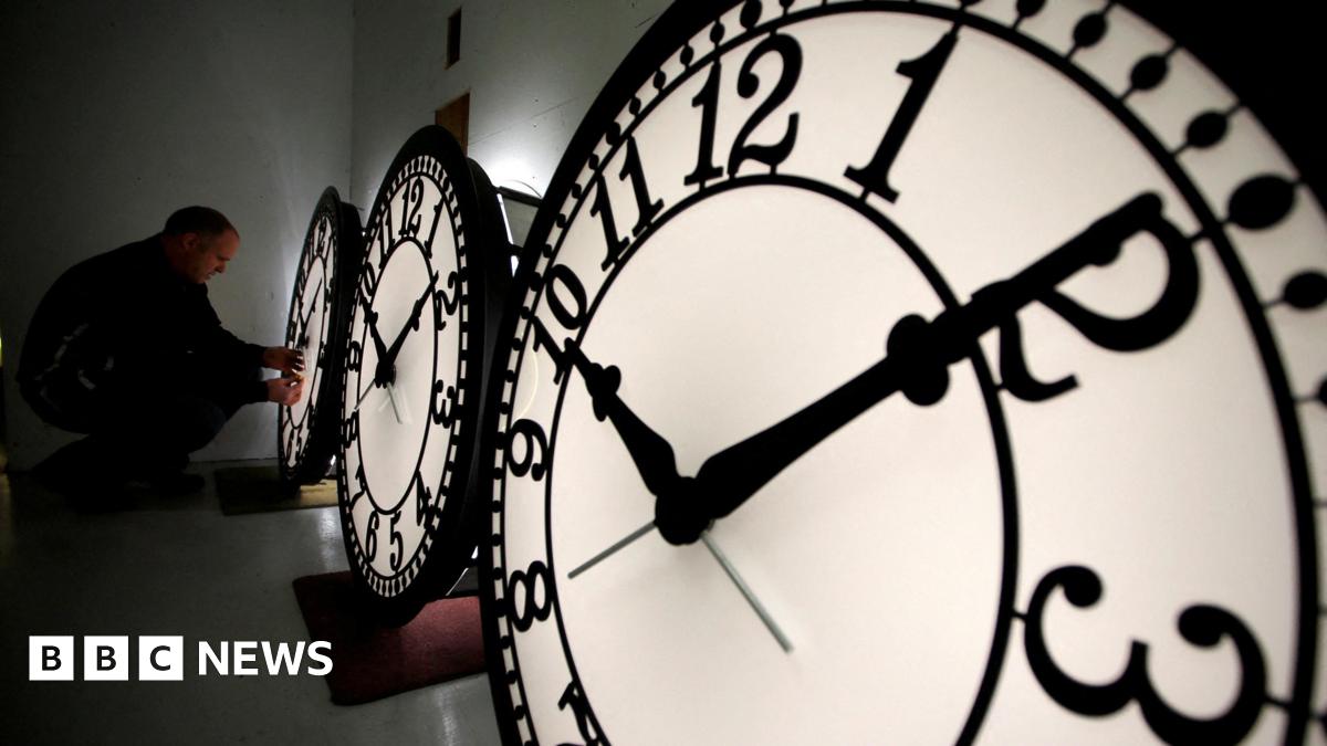 A picture of three clock faces, and a man is changing the time on the third on which is at the back of the picture.