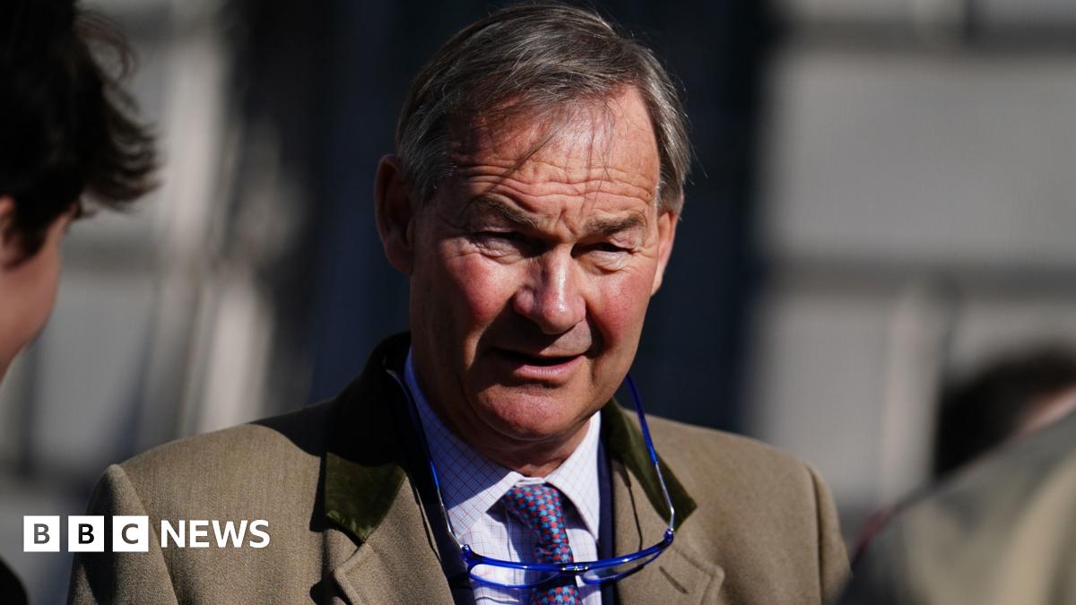 Rupert Lowe in a light brown blazer looks into the sun with a pair of glasses on a cord around his neck