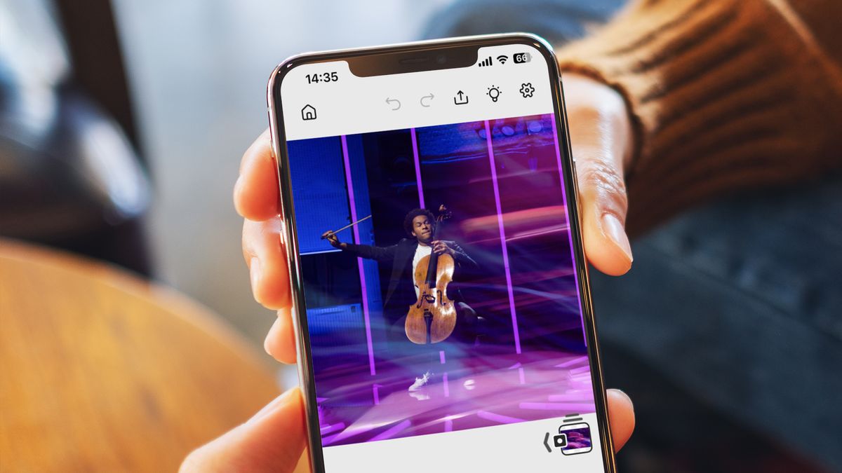 A hand holding a phone showing a photo of a musician being edited in the Photoshop for iPhone app