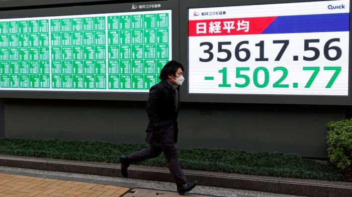 A pedestrian runs past a stock market indicator board in Tokyo