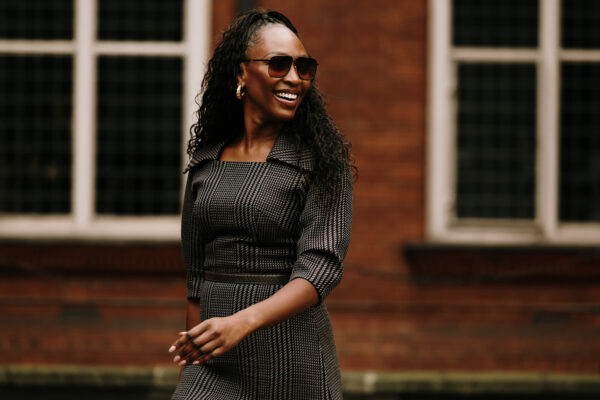 a london spring 2025 fashion week attendee smiling and wearing a checkered dress and sunglasses