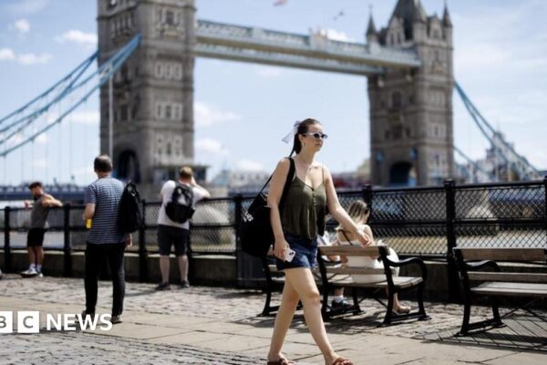 People near the River Thames during a warm day in London on 27 June 2025. A woman in shorts and a short sleeve top is at the centre of the image