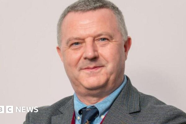 Kevin Donaghy, with grey hair, grey suit, blue shirt and blue tie.