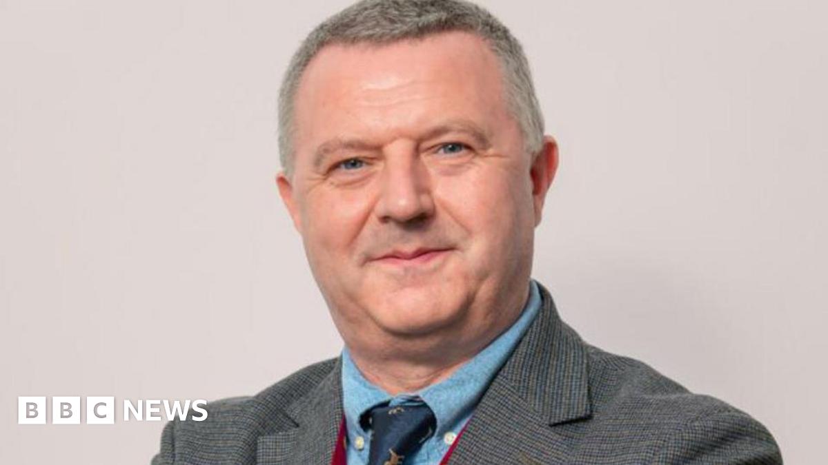 Kevin Donaghy, with grey hair, grey suit, blue shirt and blue tie.