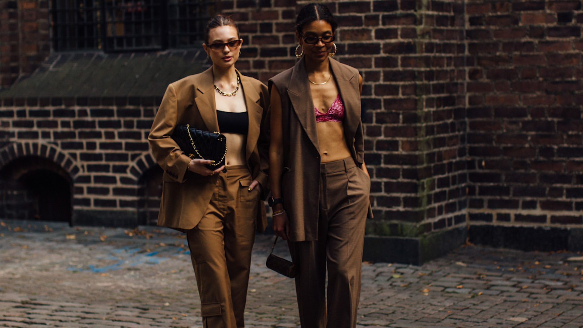 two attendees at Copenhagen spring 2023 fashion week wearing sunglasses, crop tops, and brown suits