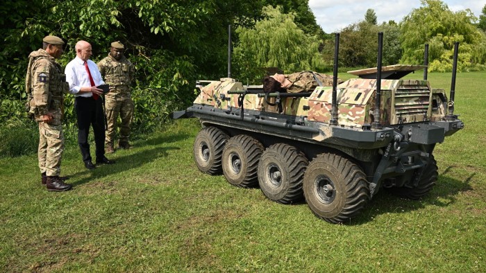 Defence secretary John Healey is flanked by two military personal as he operates an unmanned ground vehicle