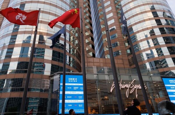 A Hong Kong and China flags next to the electronic board showing the price of the Hang Seng Index at Exchange Square in Hong Kong