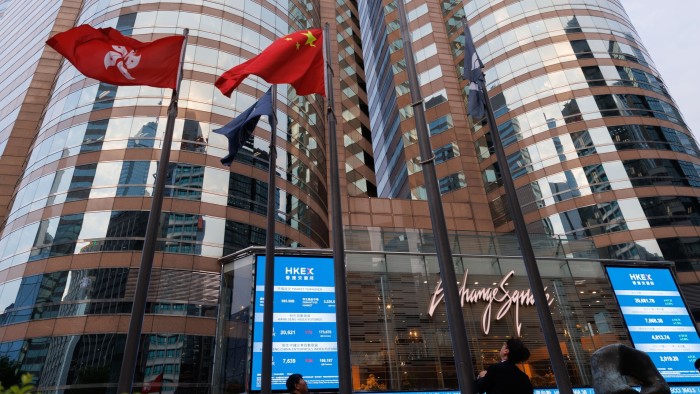 A Hong Kong and China flags next to the electronic board showing the price of the Hang Seng Index at Exchange Square in Hong Kong