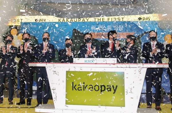 People clapping behind a podium with the Kakao Pay logo on it and confetti in the air at the payments provider’s debut on the Korea Exchange in 2021