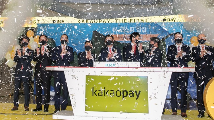 People clapping behind a podium with the Kakao Pay logo on it and confetti in the air at the payments provider’s debut on the Korea Exchange in 2021
