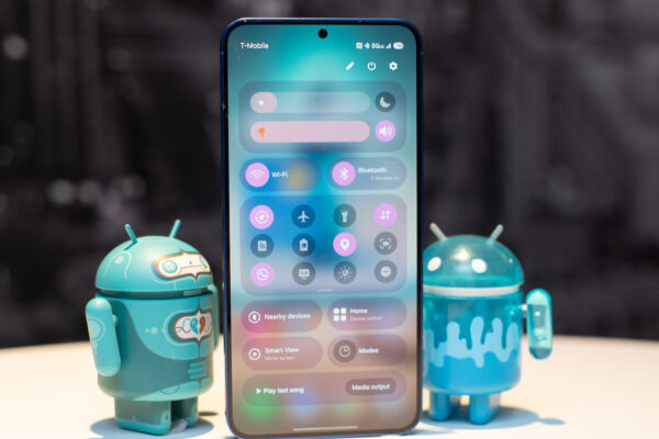 Samsung Galaxy S25 Plus in Navy Blue showing settings Quick Settings drop down, standing in between two adorable Android figurines