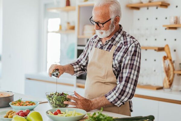 Cary Medical Center. An older man stands in a kitchen preparing a healthy meal of salad