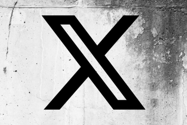 X app code points to a physical card coming to X Money X (formerly Twitter) logo on a cracked wall